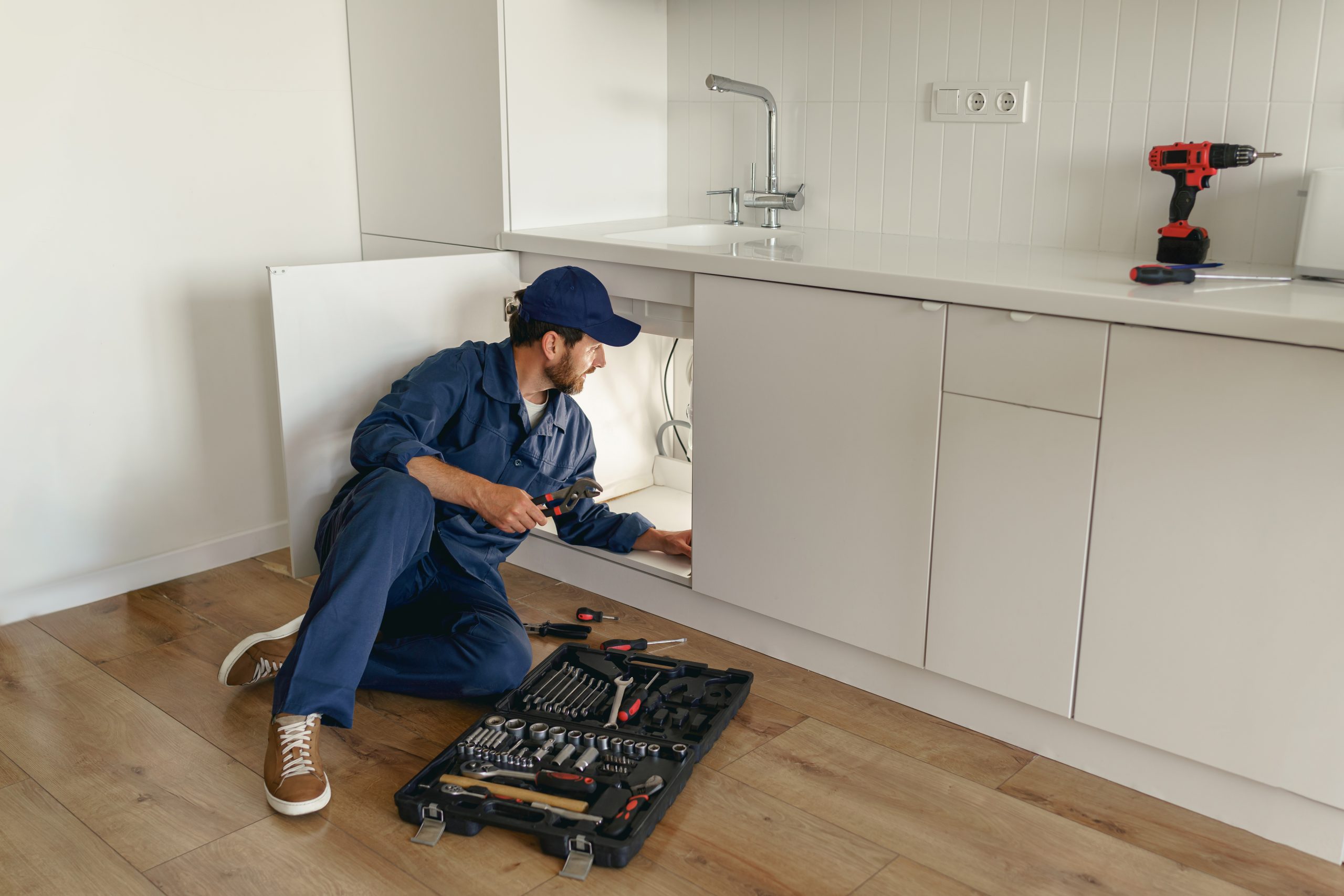 professional plumber in blue uniform fixing broken water tap in kitchen. repair service concept